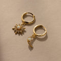 The Opal Sun & Moon Huggies feature two gold hoop earrings—one with a sunburst, one with a crescent charm—both adorned with white stones for a chic, celestial touch.