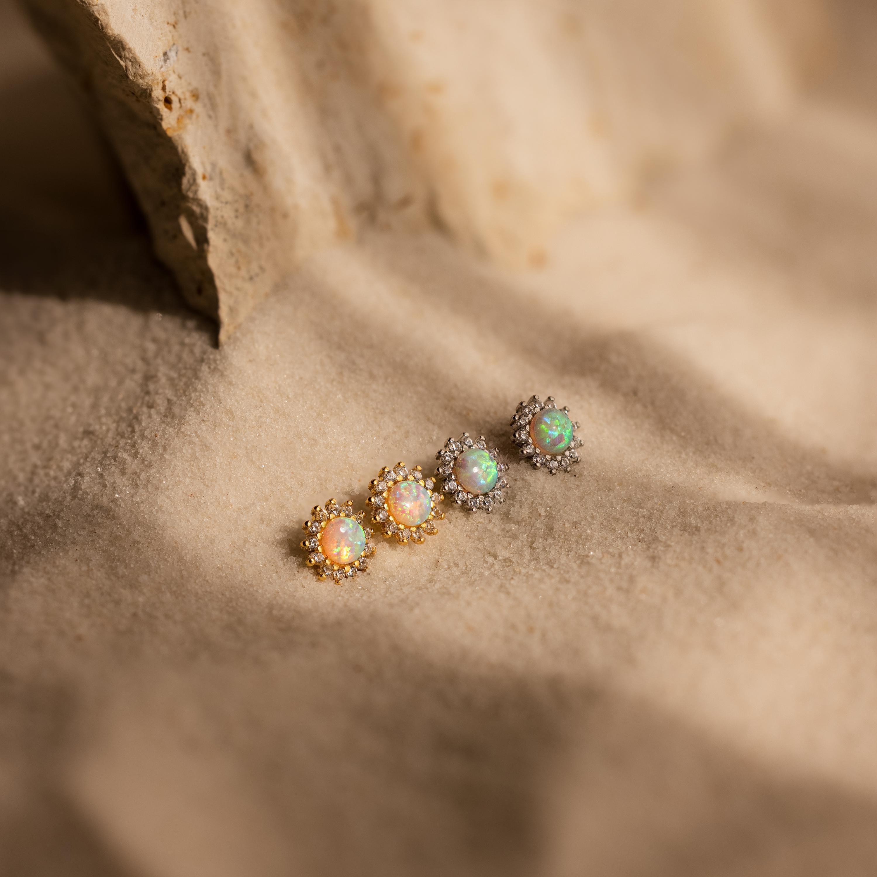 Four Pave Opal Moon Studs and diamond sparkle earrings—two pairs in gold, two in silver—displayed on textured sand, perfect for celestial jewelry lovers.