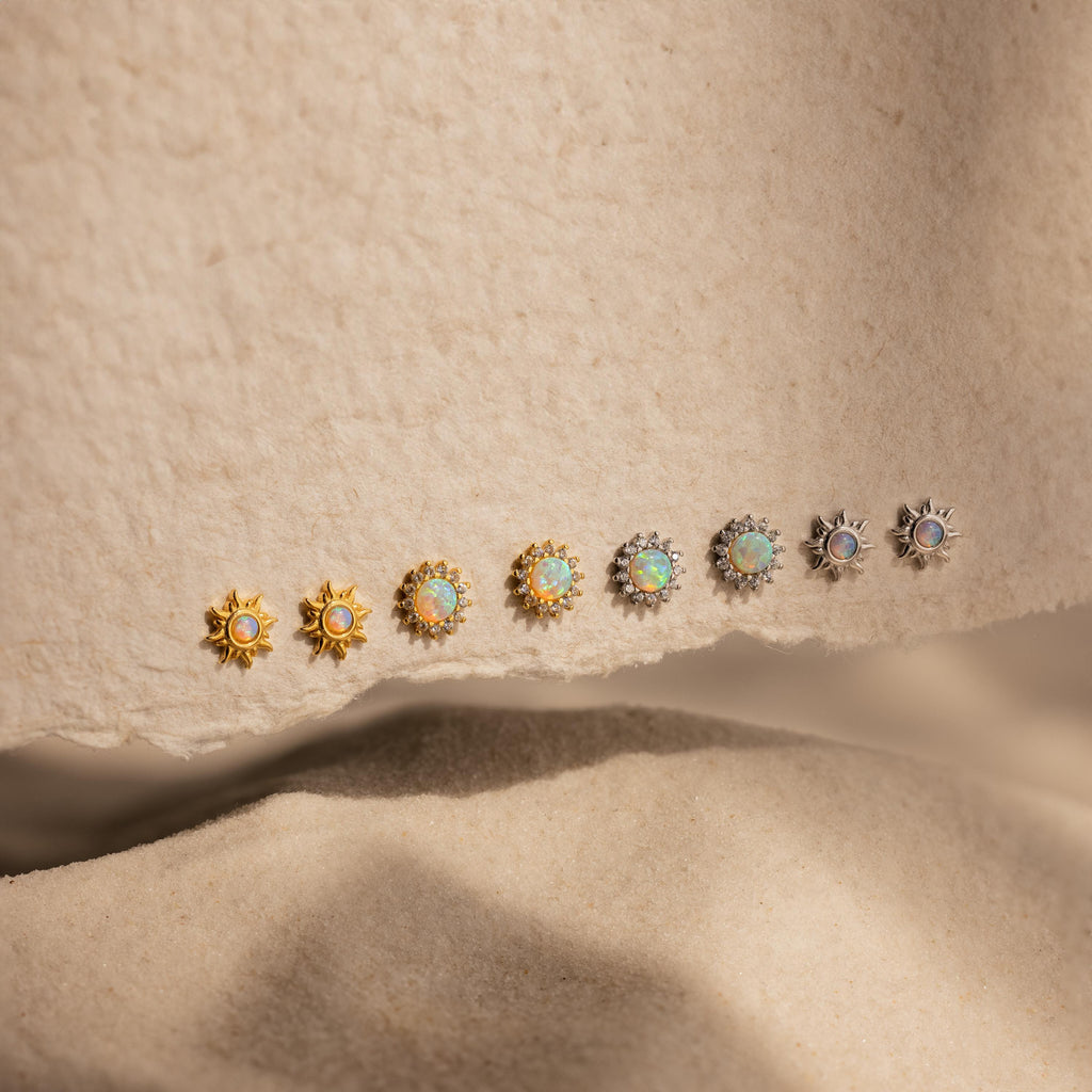 Eight pairs of Pave Opal Moon Studs in gold and silver shine with celestial sparkle on a textured beige surface.