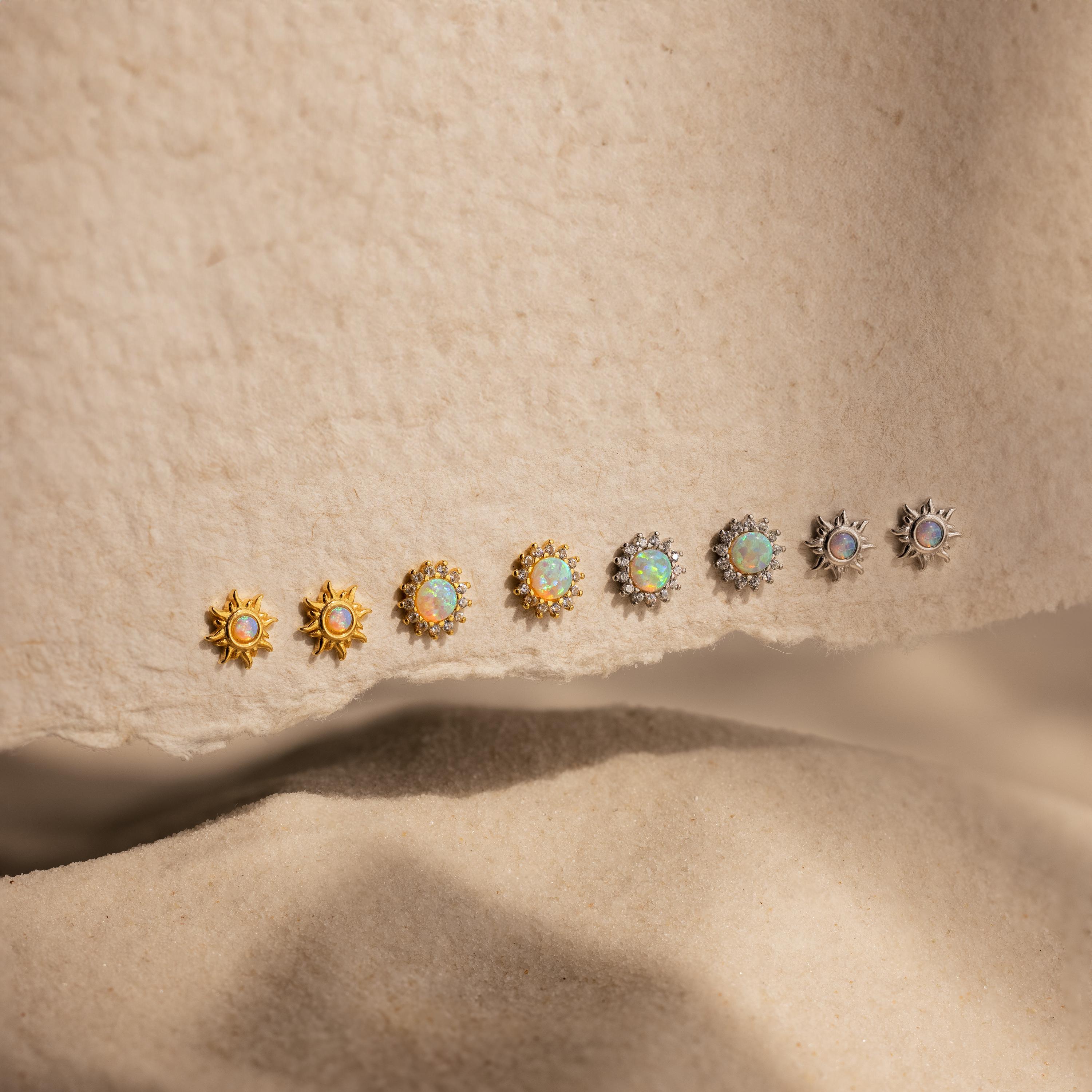 Eight pairs of Pave Opal Moon Studs in gold and silver shine with celestial sparkle on a textured beige surface.