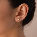 Close-up of a woman's ear wearing Pave Opal Moon Studs, featuring small round opals in a gold setting, adding a celestial jewelry charm.