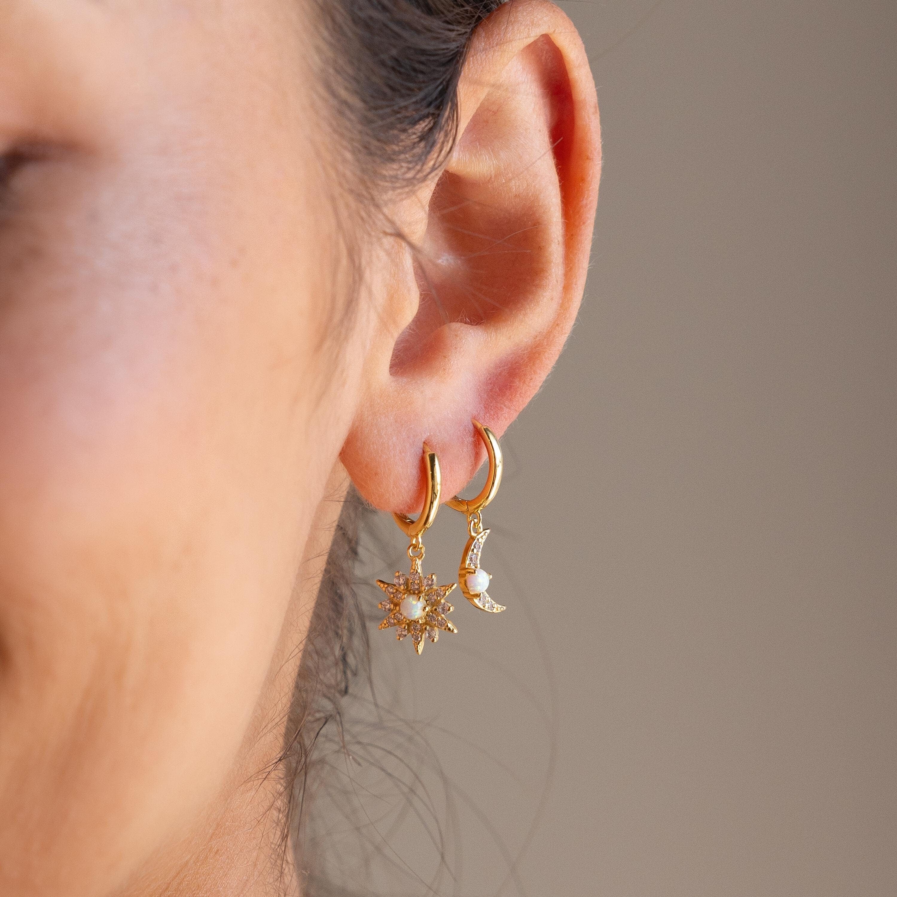Close-up of an ear wearing Opal Sun & Moon Huggies: gold hoop earrings—one with a sun charm, the other with a crescent moon—create a cosmic, stylish mismatched look.