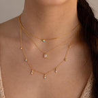 The Opal Diamond Station Necklace shines on her neck, its three gold layers with opal and gemstone pendants perfect for bridesmaids or a birthstone gift. Worn with a beige top, it highlights the necklace's elegance.