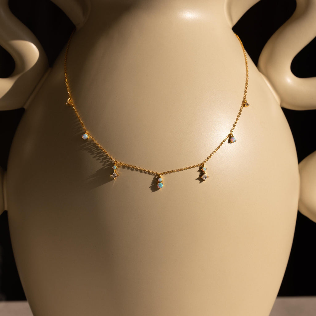 Opal Diamond Station Necklace with delicate colorful charms, ideal as a bridesmaid keepsake, elegantly displayed on a smooth, light beige vase with curved handles.