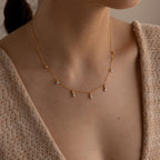 A woman wears the Opal Diamond Station Necklace with small gemstone charms and a beige knit top—an ideal birthstone gift or bridesmaid keepsake.
