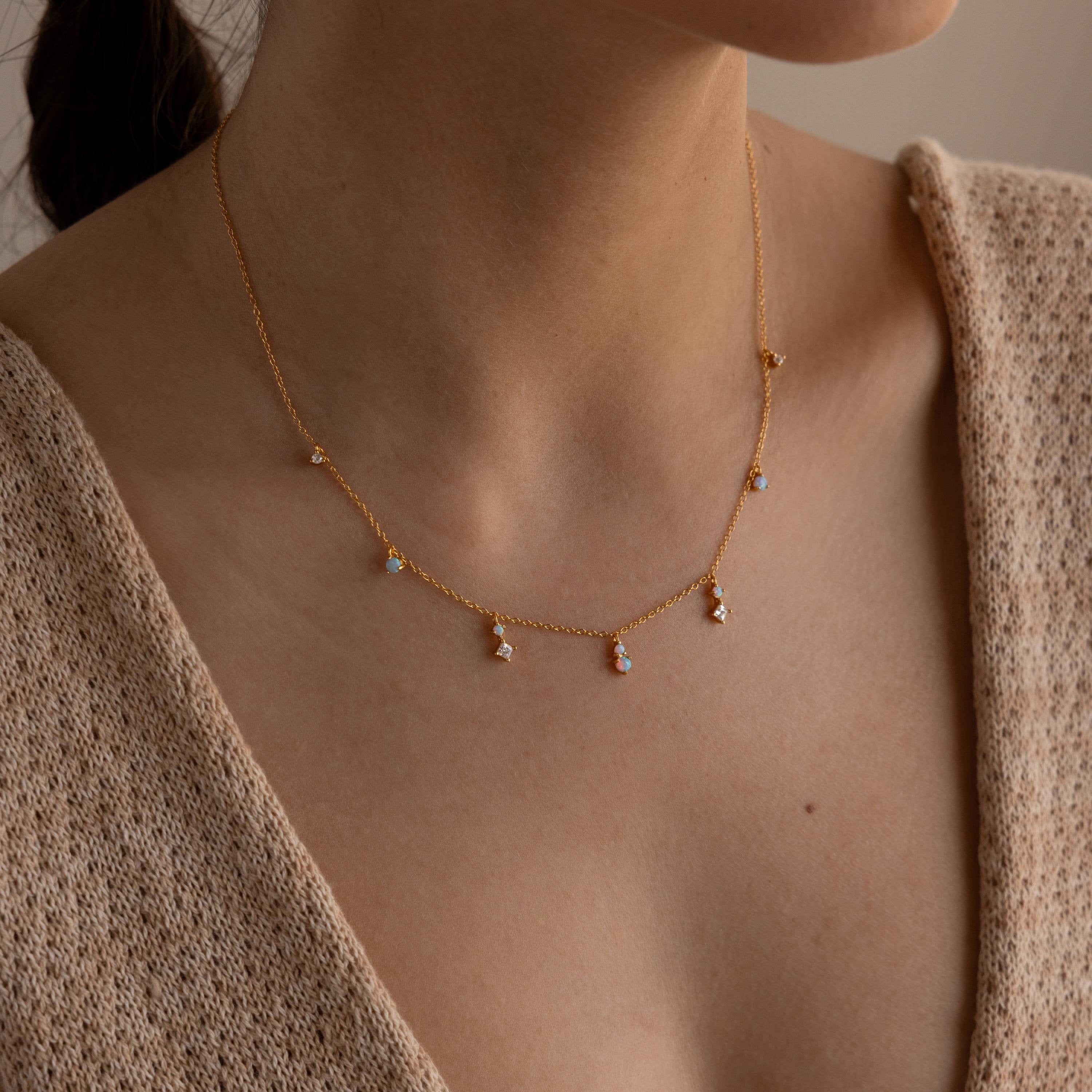 A woman wears the Opal Diamond Station Necklace with small gemstone charms and a beige knit top—an ideal birthstone gift or bridesmaid keepsake.