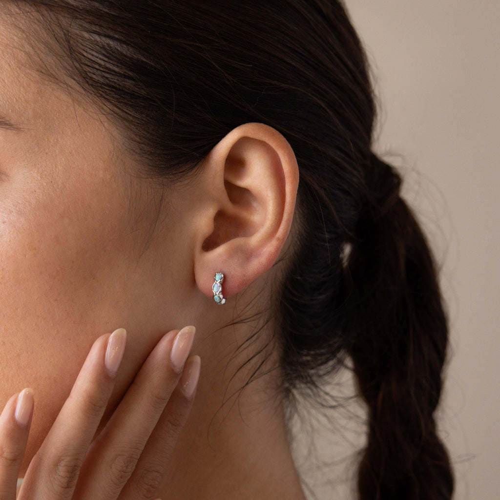 A woman with a braid touches her face, wearing Blue Opal Beaded Huggies that bring a touch of turquoise and silver to her look.