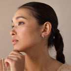 A woman with dark hair in a low ponytail looks thoughtfully to the side, wearing Blue Opal Beaded Huggies.