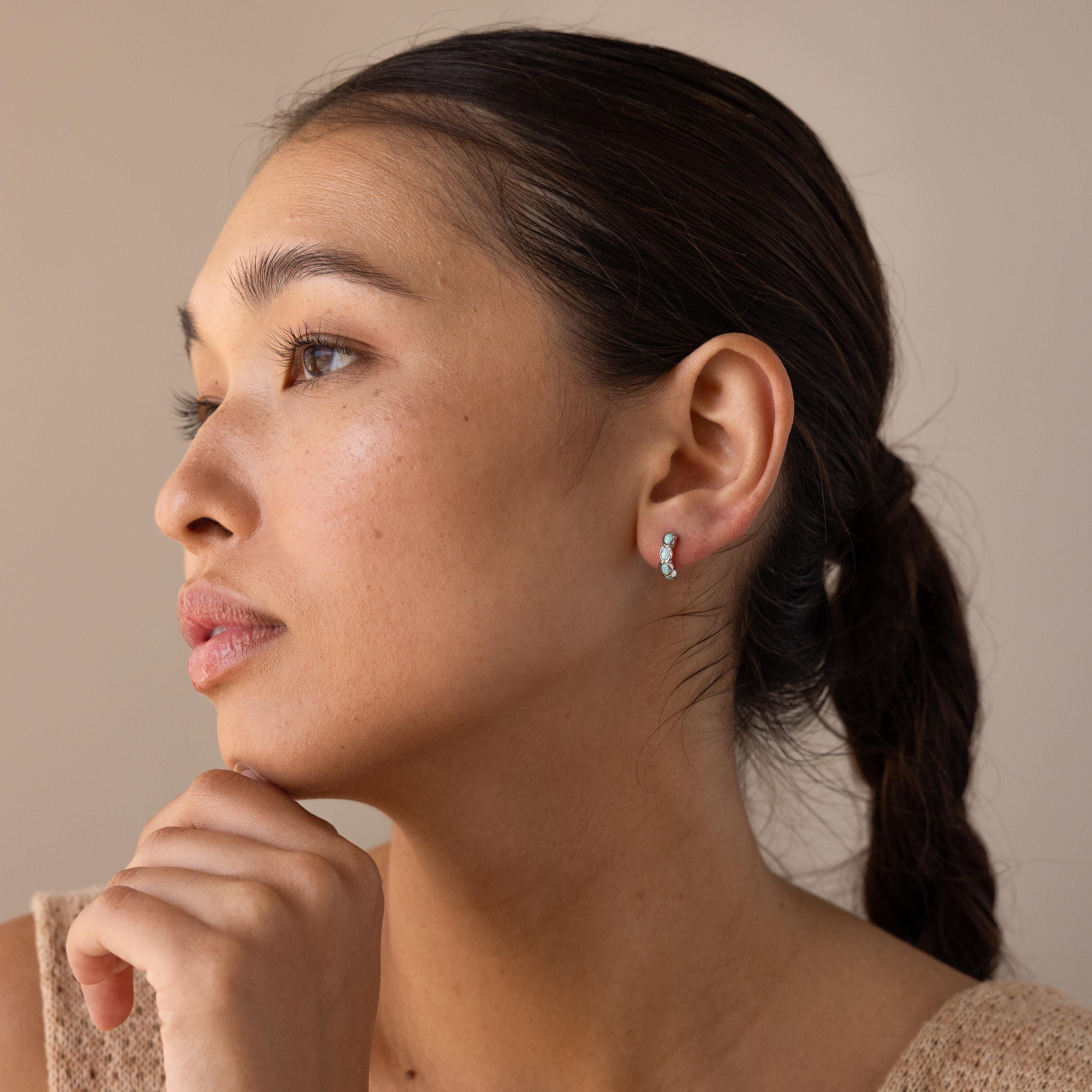 A woman with dark hair in a low ponytail looks thoughtfully to the side, wearing Blue Opal Beaded Huggies.