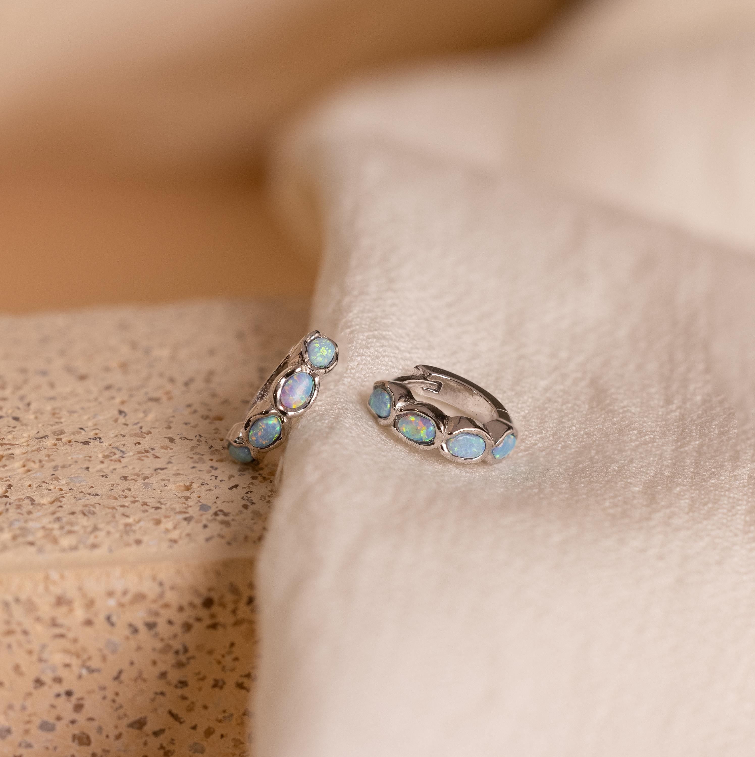 Blue Opal Beaded Huggies featuring iridescent blue opal stones on soft cream-colored fabric—these earrings make stunning birthstone gifts for any occasion.