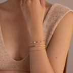 A woman wears a beige knit top and three delicate gold bracelets on her wrist, including the Opal & Diamond Cuff Bracelet featuring a small opal stone.