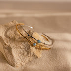 An Opal & Diamond Cuff Bracelet rests on a textured rock, its gemstones glimmering against a sandy background.