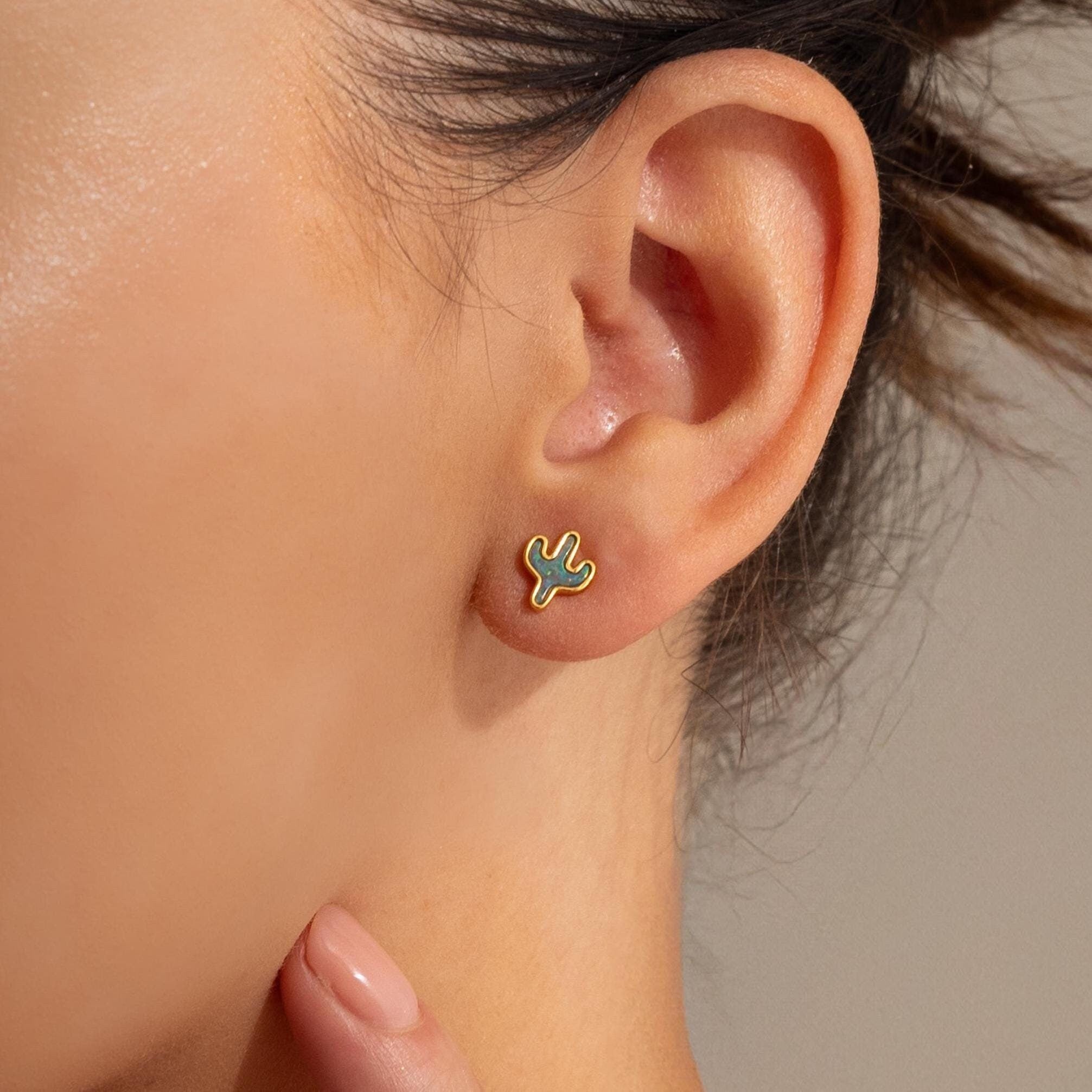 A close-up shows a hand gently touching the neck below an ear adorned with Opal Cactus Studs—distinctive green birthstone earrings.