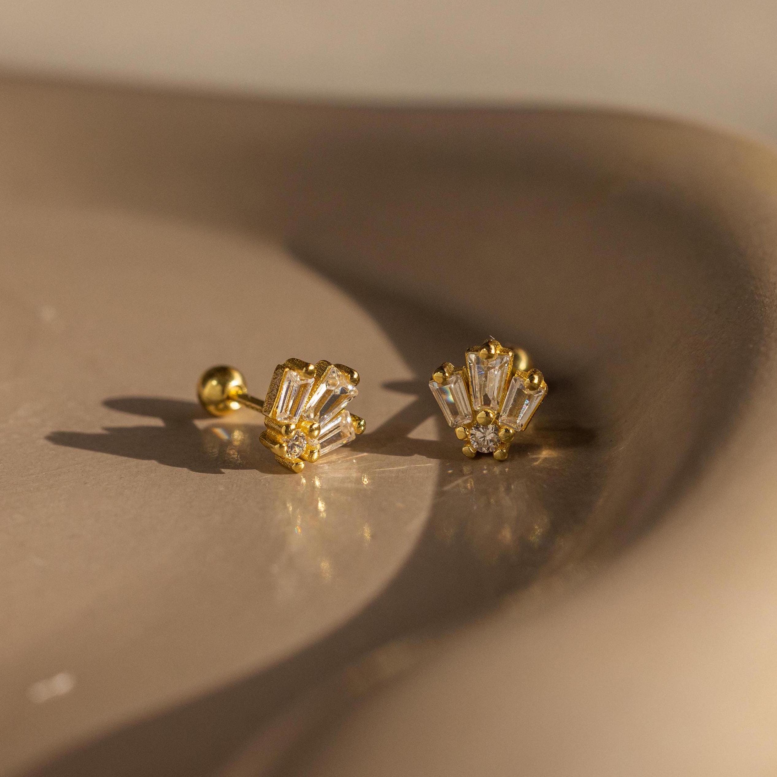 Art Deco Studs evoke vintage glamour with baguette-cut stones set in gold, showcased on a smooth beige surface under soft light.