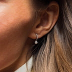 Close-up of a woman’s ear wearing Pave Pearl Drop Huggies—small hoops featuring a pearl accent and sparkling gemstones.
