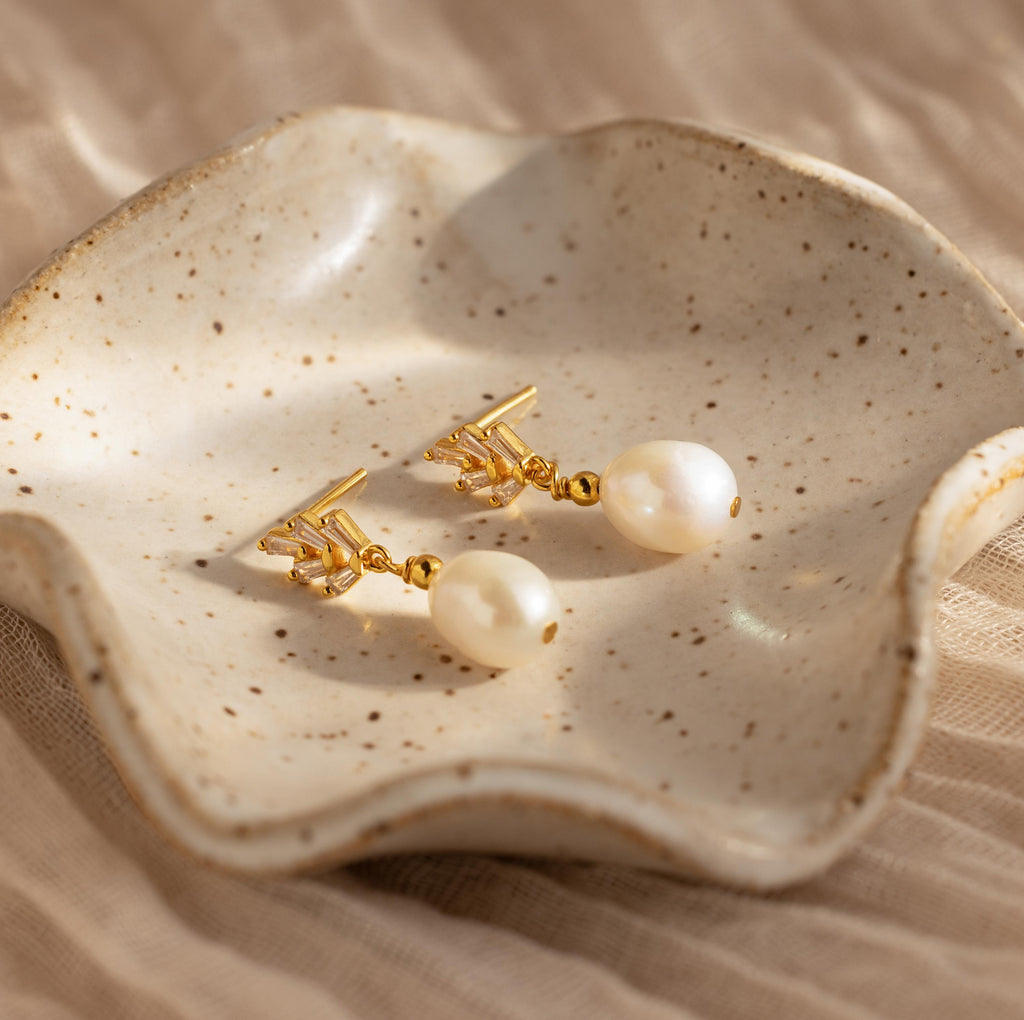 Pearl Diamond Drop Earrings are displayed on a speckled ceramic dish with wavy edges, blending modern style with a classic Art Deco-inspired design.