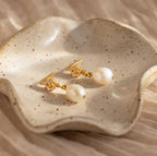 Pearl Diamond Drop Earrings are displayed on a speckled ceramic dish with wavy edges, blending modern style with a classic Art Deco-inspired design.