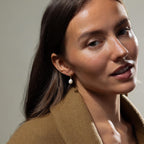Woman with long brown hair wearing a tan coat and Pearl Diamond Drop Earrings, looking at the camera.