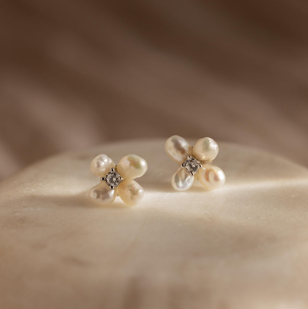 Pearl Flower Studs featuring a floral design with pearls and crystals, elegantly displayed on a soft beige surface under gentle lighting.
