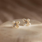 Pearl Flower Studs featuring a floral design with pearls and crystals, elegantly displayed on a soft beige surface under gentle lighting.