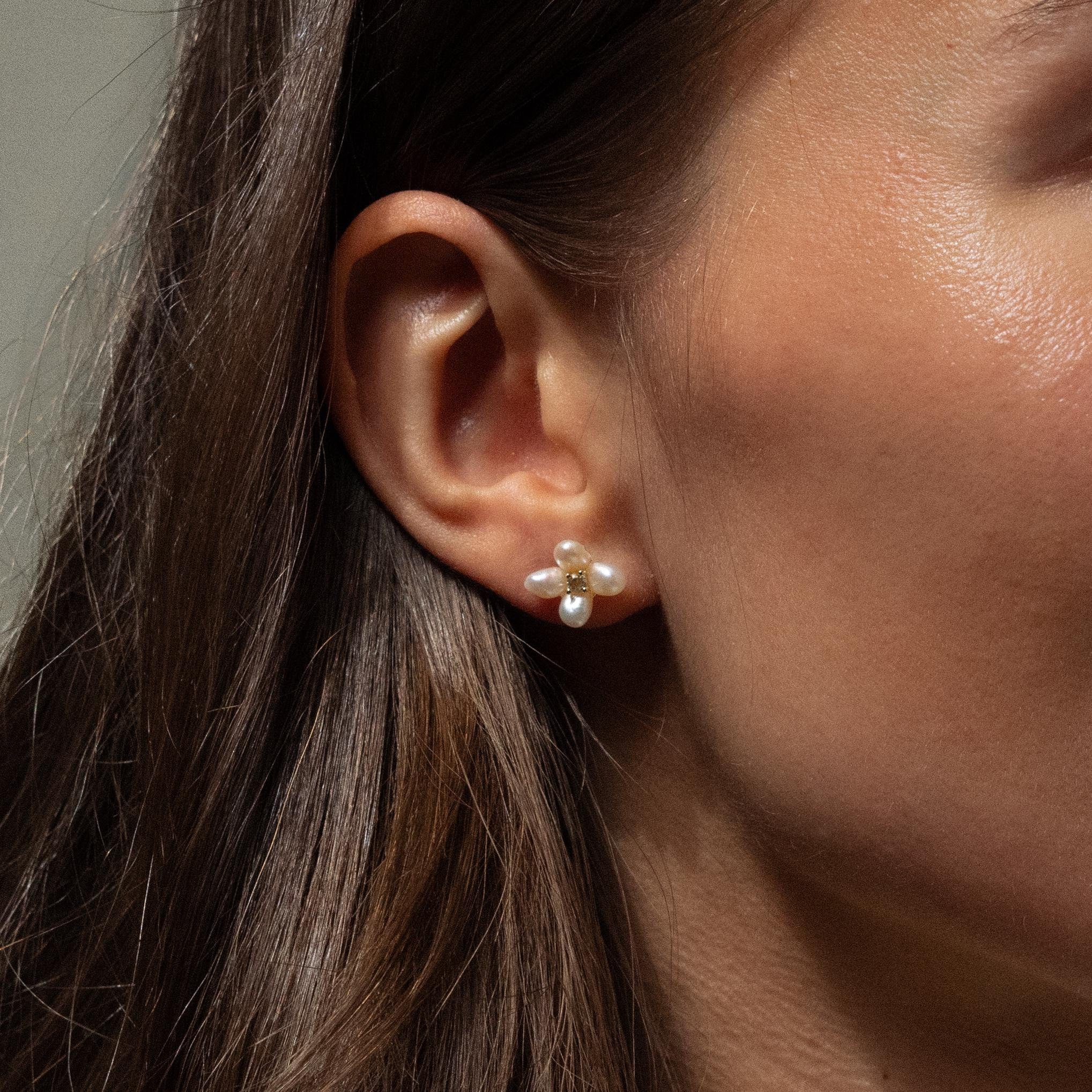 Close-up of a woman's ear wearing Pearl Flower Studs—gold and pearl earrings with a floral design that add delicate elegance.