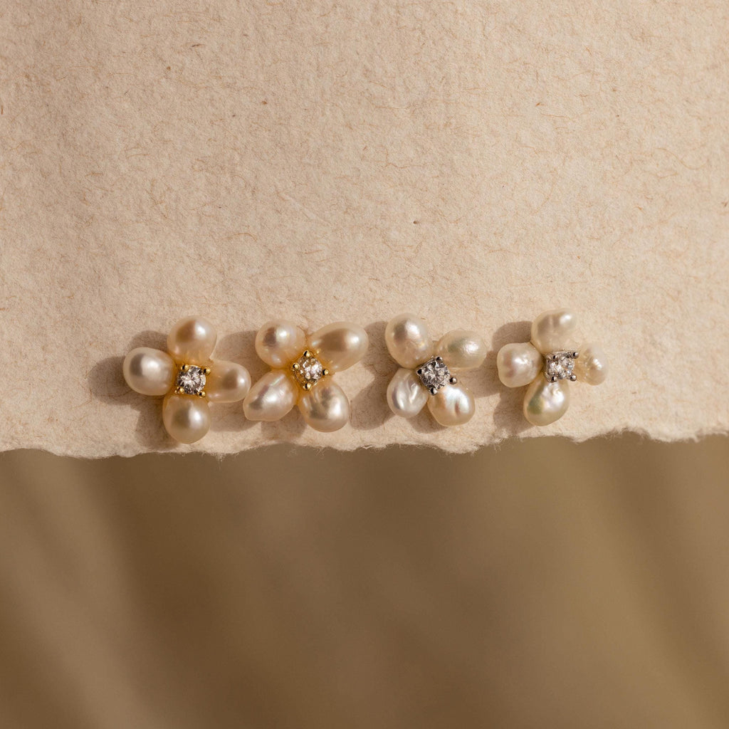 Four Pearl Flower Studs, each featuring a gemstone center, are displayed on textured beige paper to showcase the refined elegance of these floral-inspired earrings.