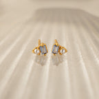 Pearl Aquamarine Studs feature rectangular aquamarine gemstones and small pearls set in gold, elegantly displayed on a textured beige surface—perfect for any occasion.