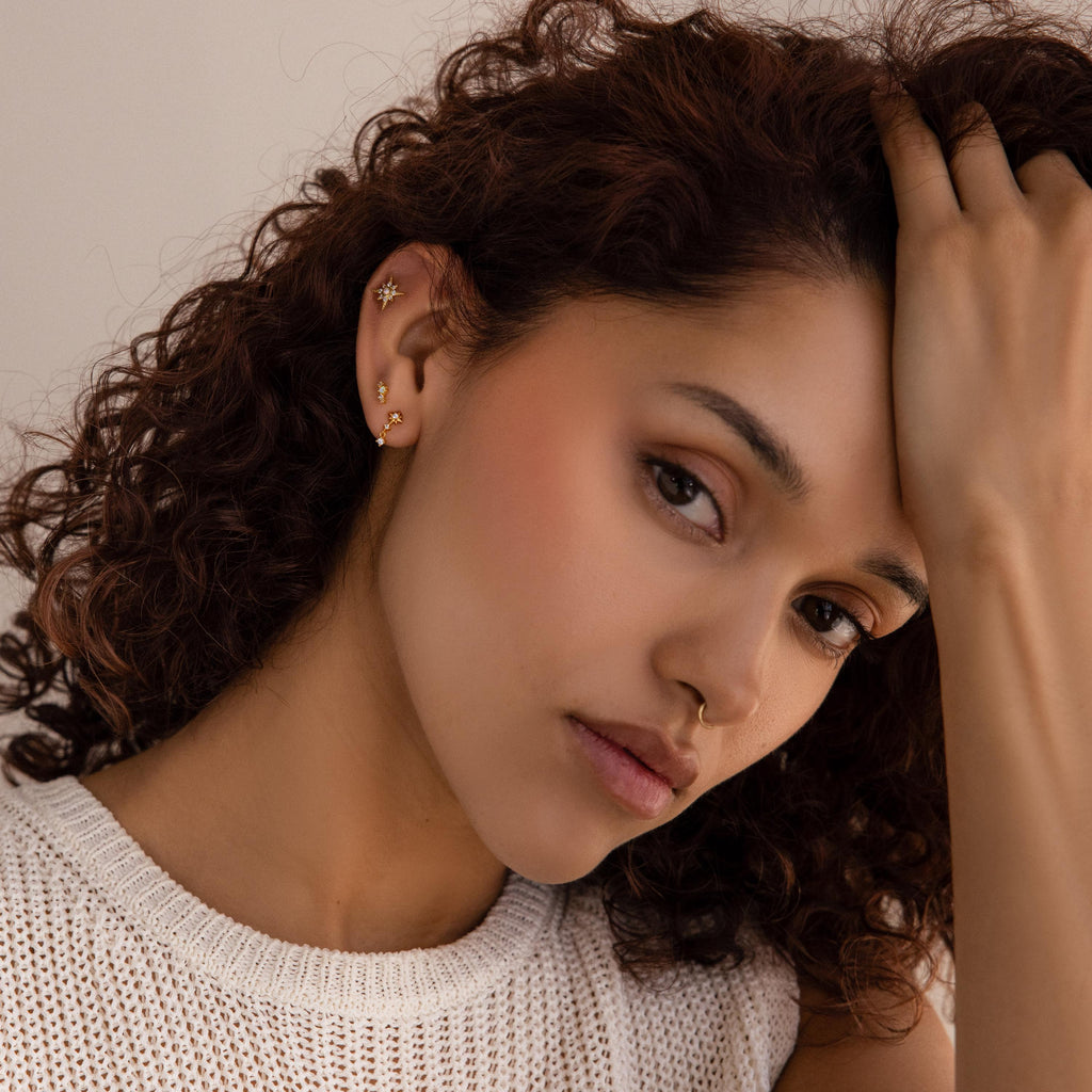 A woman with curly hair poses in a white knit top, wearing Diamond Starburst Drop Studs.