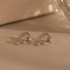 Diamond Starburst Drop Studs in Sterling Silver, star-shaped earrings with sparkling gems, are displayed on a neutral beige surface.