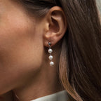 Close-up of a woman's ear wearing "Dainty Pearl Drop Studs"—elegant silver earrings featuring three dangling white pearls.