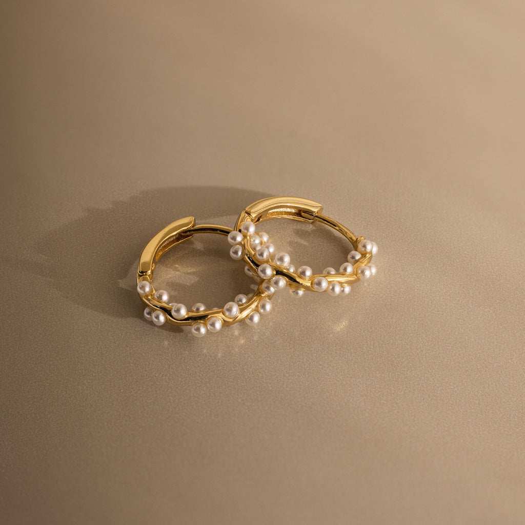 Pearl Cluster Huggies featuring delicate white pearls, displayed on a smooth beige surface—elegant earrings perfect for bridal wear or any special occasion.