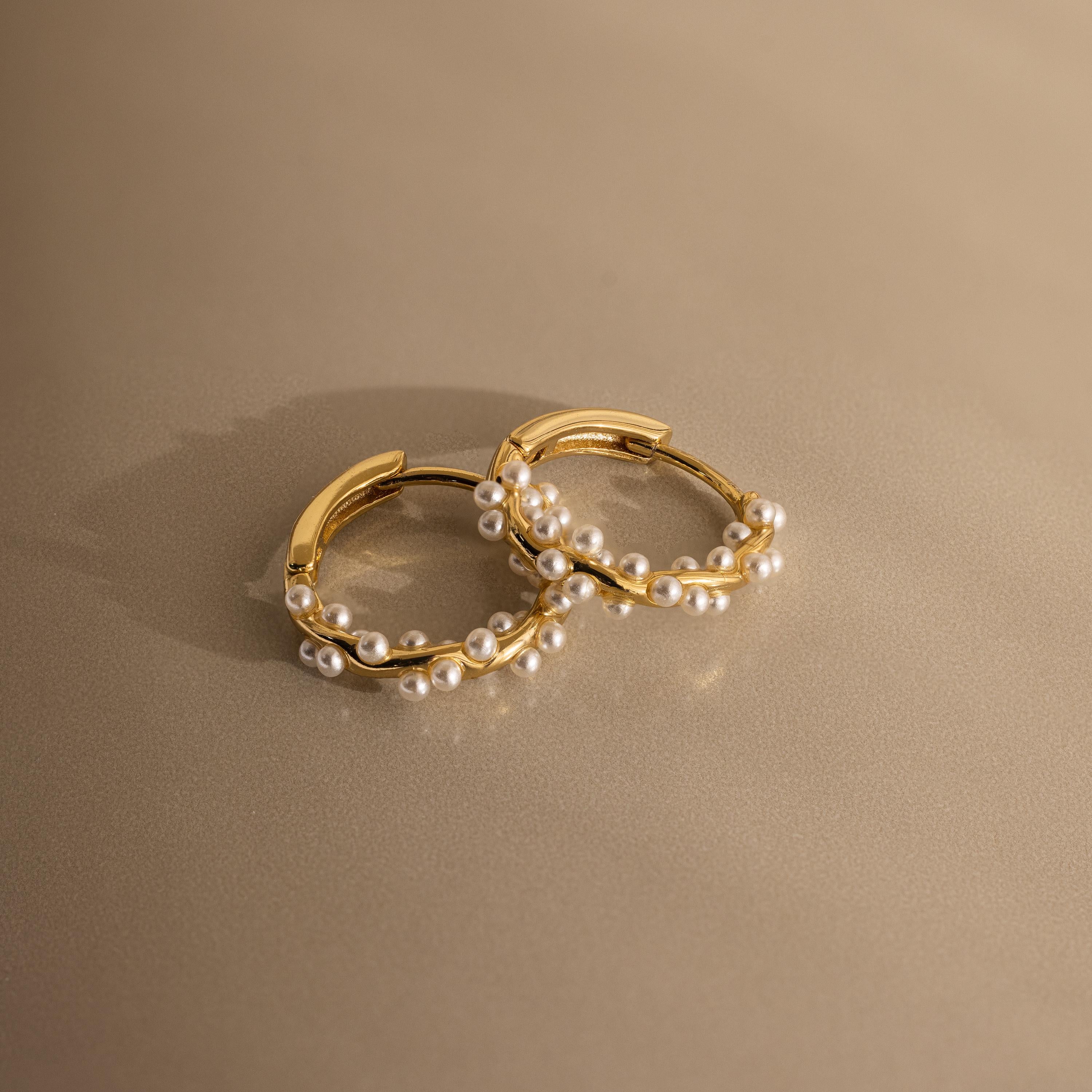 Pearl Cluster Huggies featuring delicate white pearls, displayed on a smooth beige surface—elegant earrings perfect for bridal wear or any special occasion.