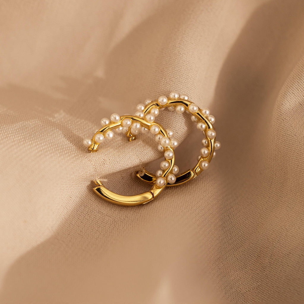 Pearl Cluster Huggies—gold hoop earrings embellished with delicate pearls, shown on beige fabric—make elegant bridal jewelry or a stylish accessory for any occasion.
