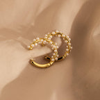 Pearl Cluster Huggies—gold hoop earrings embellished with delicate pearls, shown on beige fabric—make elegant bridal jewelry or a stylish accessory for any occasion.