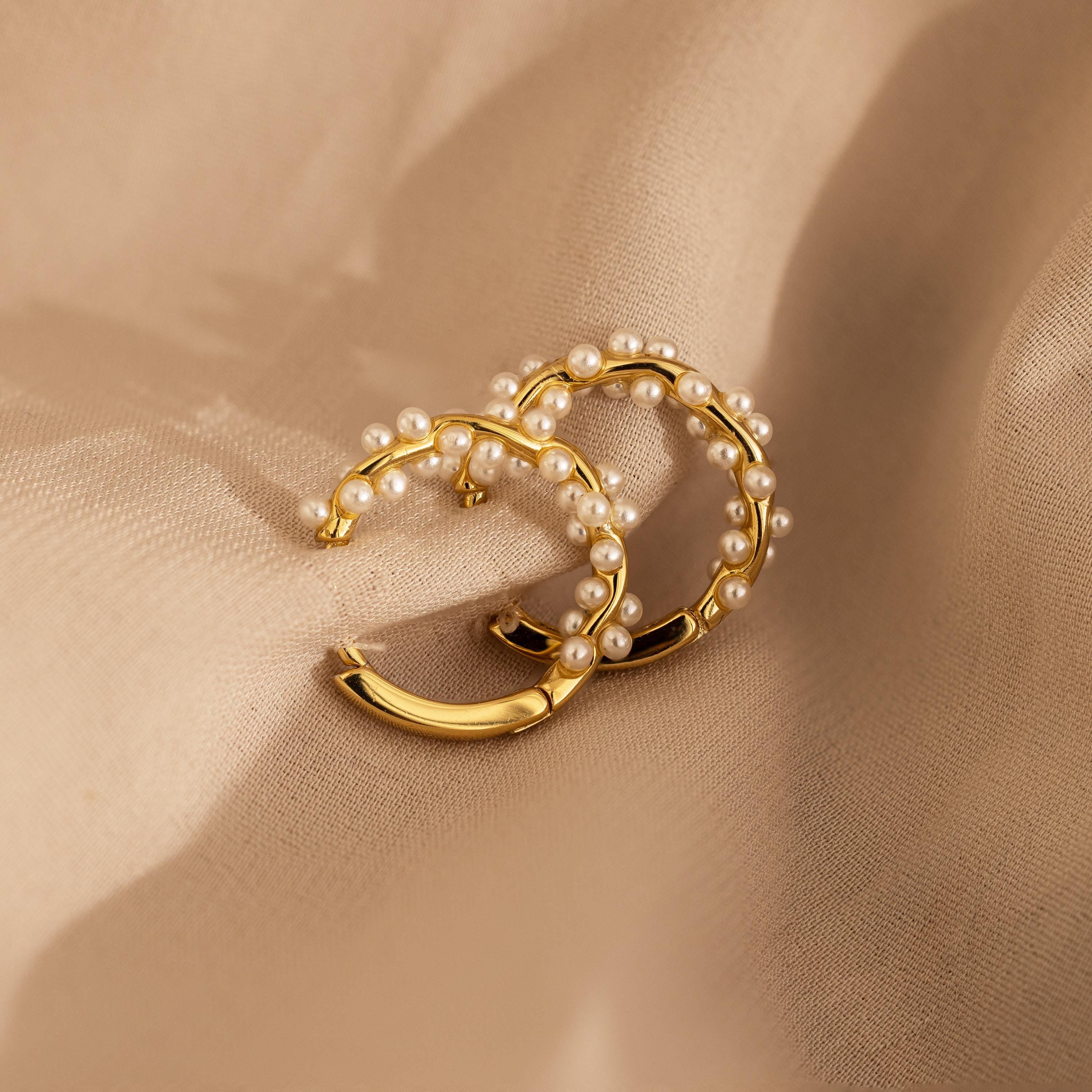 Pearl Cluster Huggies—gold hoop earrings embellished with delicate pearls, shown on beige fabric—make elegant bridal jewelry or a stylish accessory for any occasion.