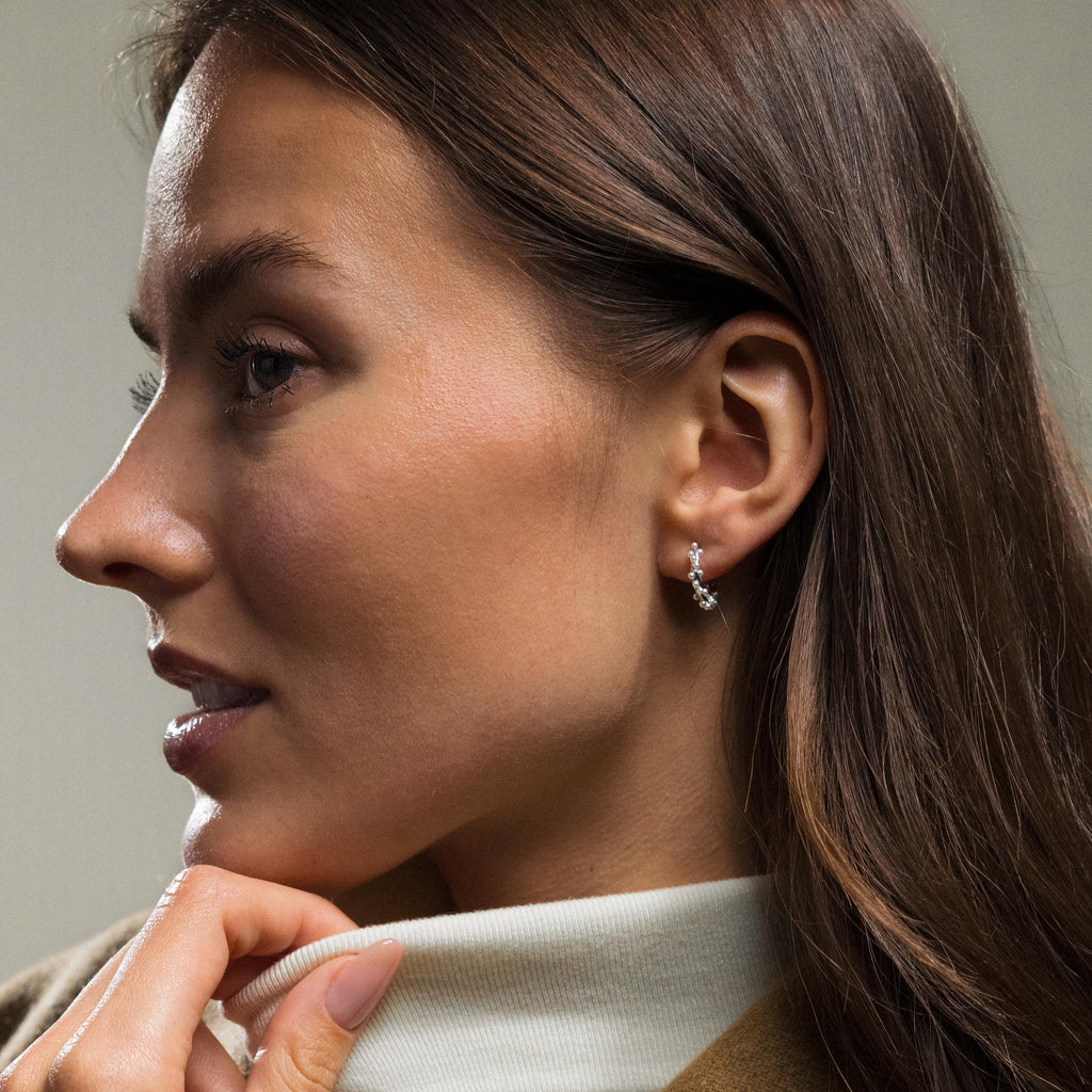 Woman with long brown hair wears a light turtleneck sweater and Pearl Cluster Huggies in Sterling Silver.