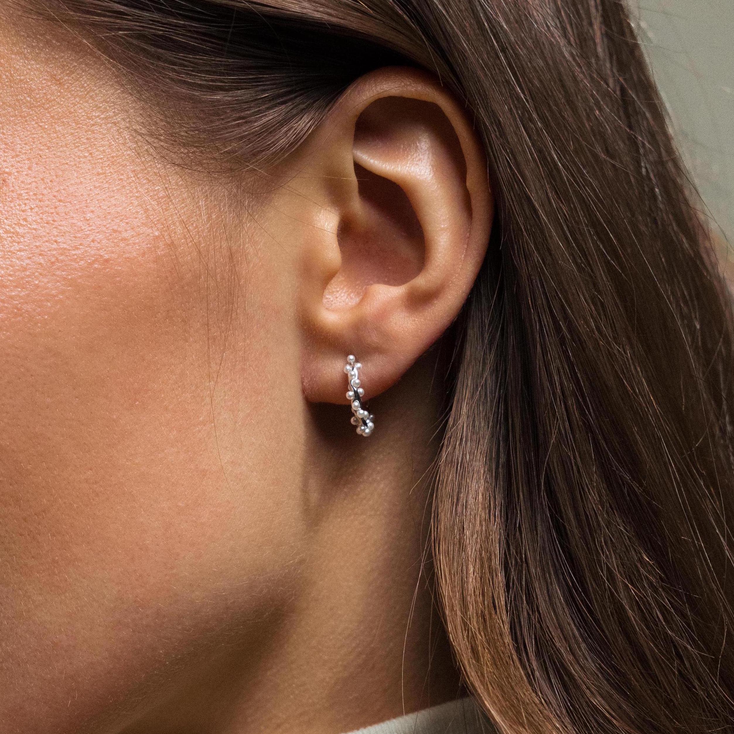 A close-up of a woman's ear adorned with Pearl Cluster Huggies in Sterling Silver.
