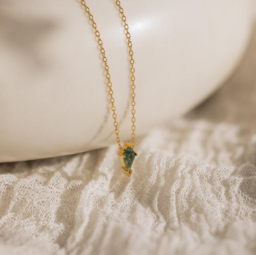 Gold chain necklace featuring a green agate Art Deco pendant, displayed on a textured ivory fabric background.