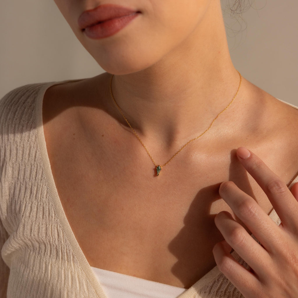 A woman in a cream top touches her collarbone while wearing the Agate Art Deco Pendant Necklace.