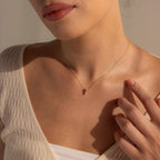 A woman in a cream top touches her collarbone while wearing the Agate Art Deco Pendant Necklace.