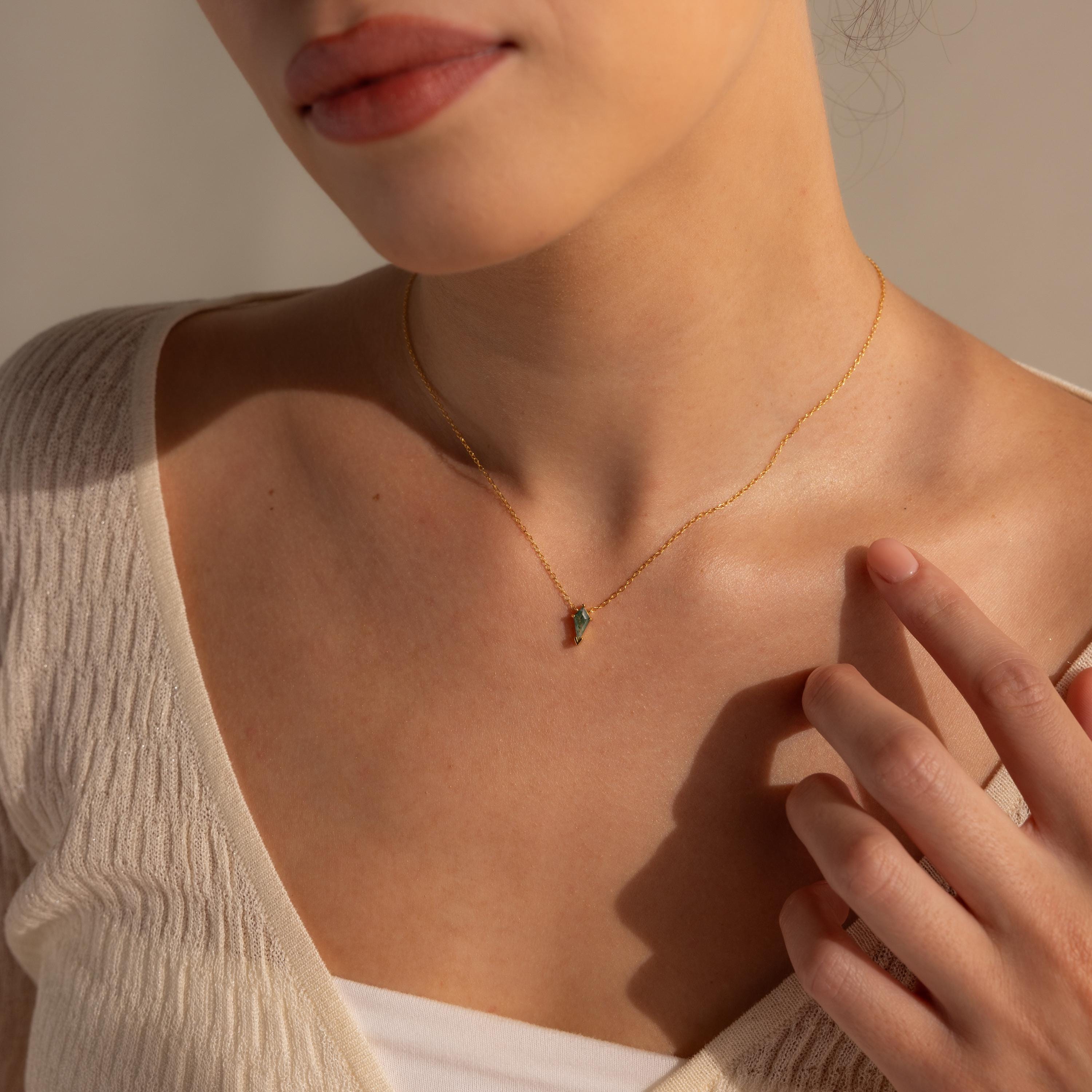 A woman in a cream top touches her collarbone while wearing the Agate Art Deco Pendant Necklace.