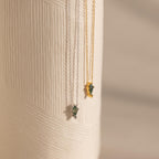 Two Agate Art Deco Pendant Necklaces—one silver, one gold—feature striking green moss agate pendants and hang elegantly against a textured white surface.