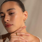 A woman poses for a photo, elegantly showcasing the Art Deco Diamond Tag Huggies—vintage-inspired hoops adorned with sparkling baguette-cut diamonds.