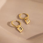 Art Deco Diamond Tag Huggies: Gold vintage-inspired hoops featuring square, diamond-accented charms set against a soft beige background.