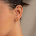Close-up of a woman's ear wearing two gold earrings: a small stud and the Dangling Diamond Chain Huggies inspired by art deco jewelry.