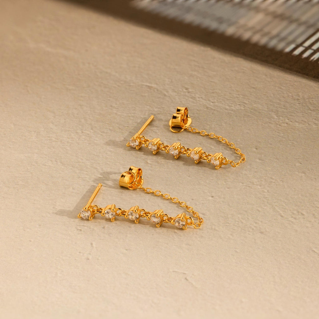 Diamond Chain Drop Earrings with sparkling stones, beautifully displayed on a beige textured surface. A charming gift for her.