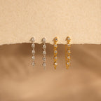 Two pairs of Diamond Chain Drop Earrings, one in silver and one in gold, displayed on a textured beige surface—a perfect sparkling gift for her.