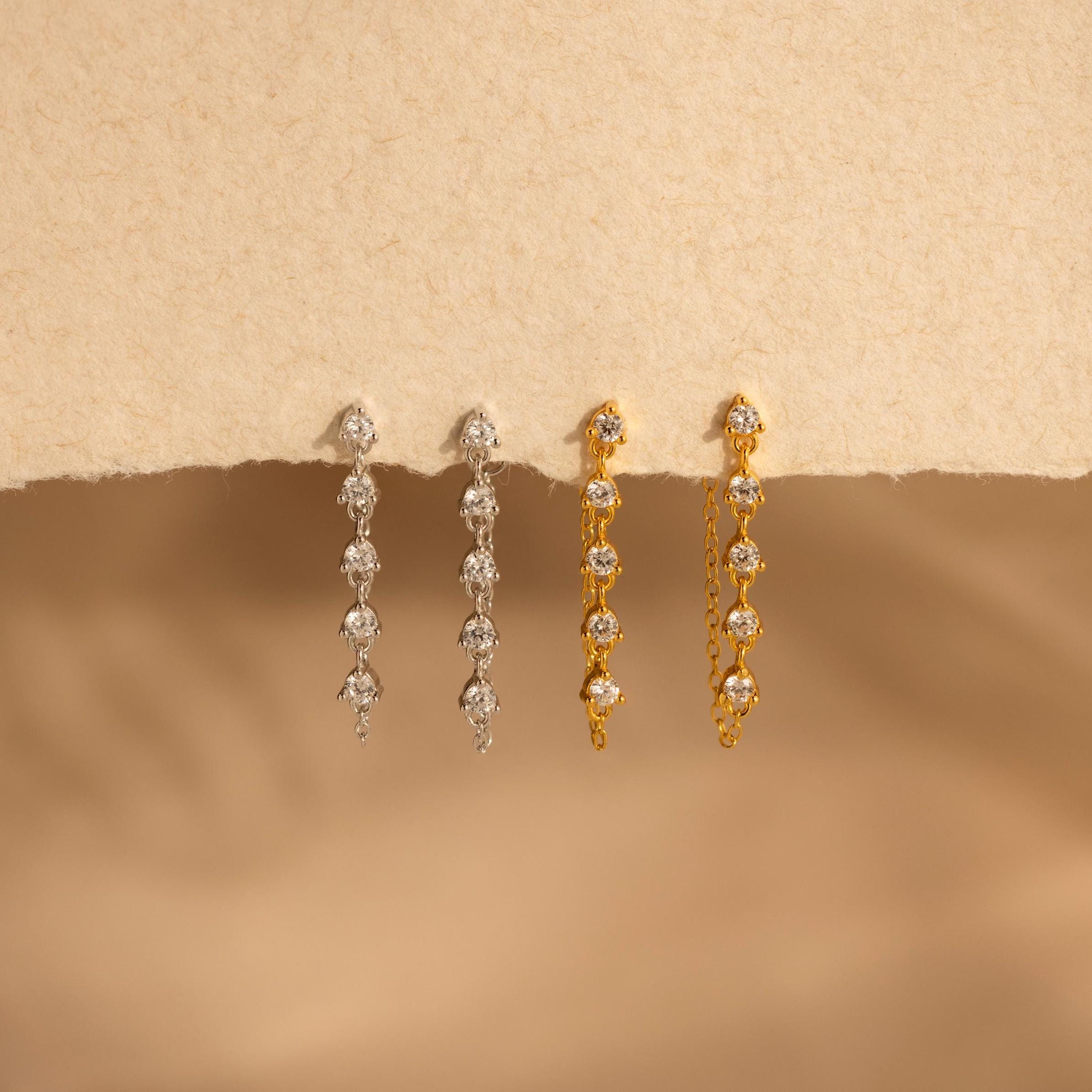 Two pairs of Diamond Chain Drop Earrings, one in silver and one in gold, displayed on a textured beige surface—a perfect sparkling gift for her.