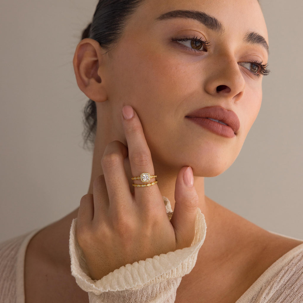 A woman with natural makeup touches her face, showcasing the Vintage Diamond Rings Set with a cushion-cut halo and marquise-detailed band on her finger.