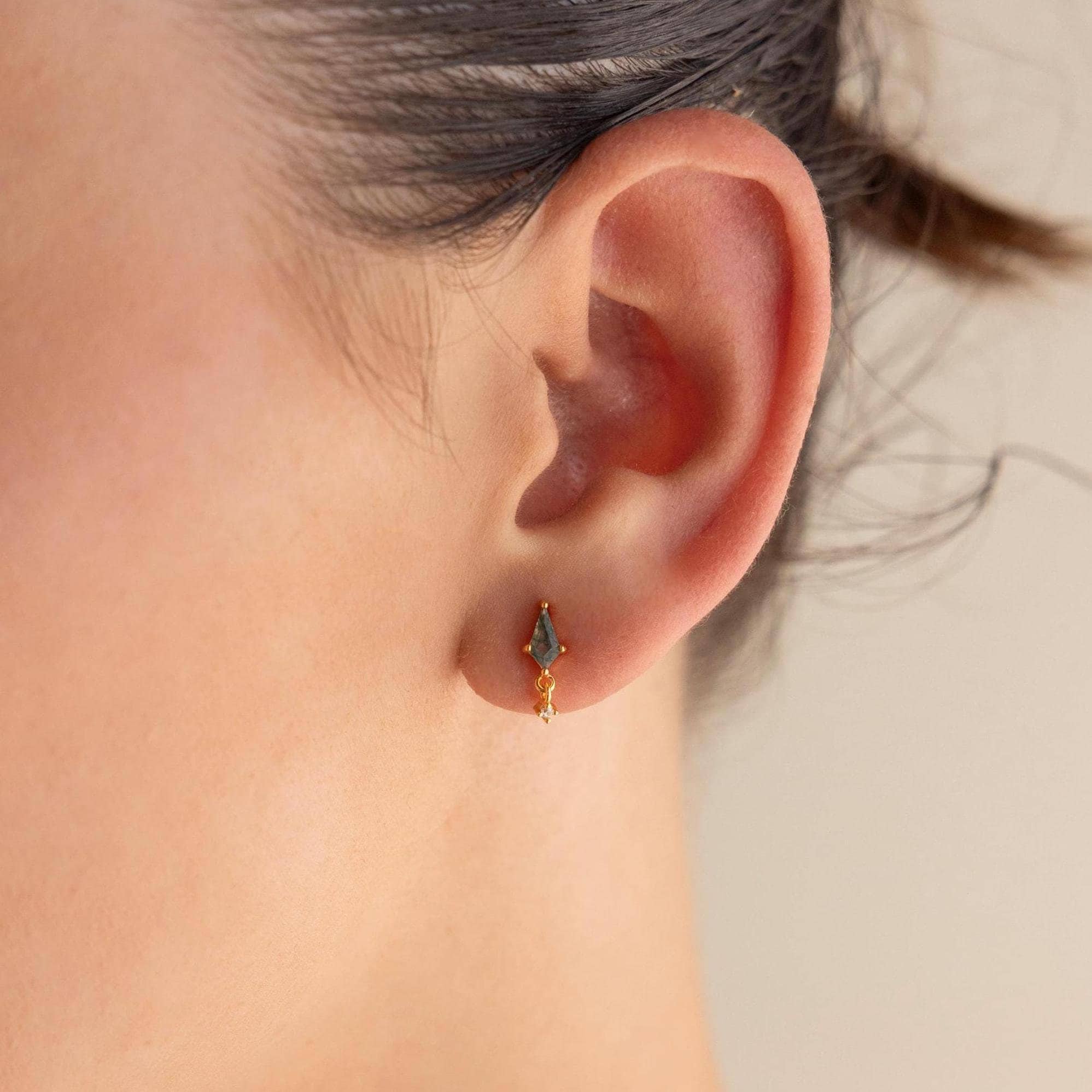 Close-up of a woman's ear wearing the Agate Kite Drop Earrings, featuring small geometric studs accented with sparkling moss agate and a delicate diamond charm.